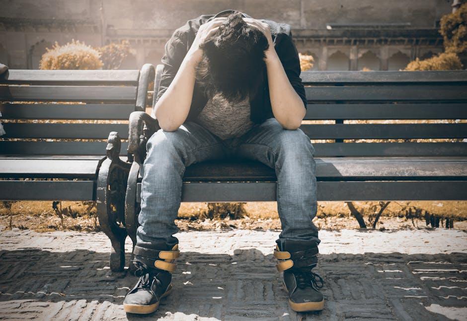 Man in Black Shirt and Gray Denim Pants Sitting on Gray Padded Bench